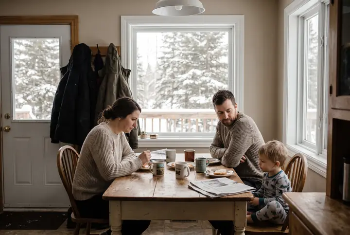 A family at a wooden kitchen table in winter morning light.